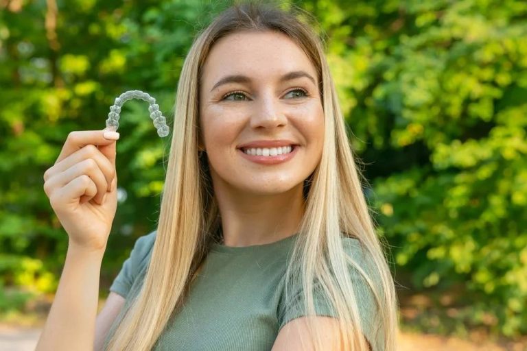 Young woman holding a clear orthodontic aligner against green foliage backdrop